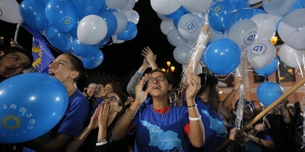 Mehrere junge Menschen in blauen T-Shirts applaudieren und halten mit Hellium gefüllte, blaue und weiße Luftballons Mehrere junge Menschen in blauen T-Shirts applaudieren und halten mit Hellium gefüllte, blaue und weiße Luftballons