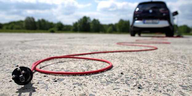 Ein rotes Kabel zum Laden eines E-Autos, das im Hintergrund zu sehen ist, liegt auf dem Boden Ein rotes Kabel zum Laden eines E-Autos, das im Hintergrund zu sehen ist, liegt auf dem Boden