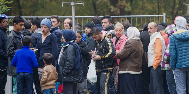 Menschen warten vor einem Zaum Menschen warten vor einem Zaum