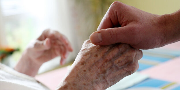 Eine Hand hält die einer bettlägerigen Seniorin Eine Hand hält die einer bettlägerigen Seniorin
