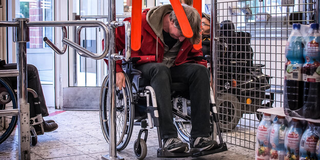 Ein Mann passiert im Rollstuhl eine Einkaufswagen-Schranke in einem Supermarkt Ein Mann passiert im Rollstuhl eine Einkaufswagen-Schranke in einem Supermarkt