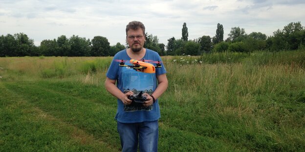Ein Mann mit Brille und Bart steuert auf einem Feld einen kleinen Copter mit vier Rotoren Ein Mann mit Brille und Bart steuert auf einem Feld einen kleinen Copter mit vier Rotoren