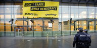 An einem Gebäude hängt ein Plakat „Don't tade away democracy #Stopceta Greenpeace“, zwei Polizisten blicken darauf