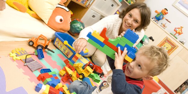 Ein Kind spielt mit Bauklötzen, daneben sitzt eine Frau Ein Kind spielt mit Bauklötzen, daneben sitzt eine Frau