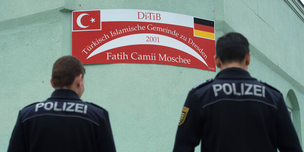 Zwei Polizisten stehen mit dem Rücken zum Betrachter vor der Mauer einer Moschee Zwei Polizisten stehen mit dem Rücken zum Betrachter vor der Mauer einer Moschee