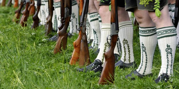 Männerbeine in bestickten Traditionssocken, davor stehen Gewehr Männerbeine in bestickten Traditionssocken, davor stehen Gewehr