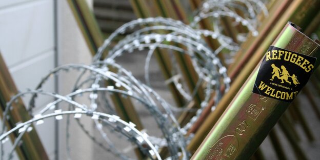 Ein Stacheldrahtzaun. Darauf klebt ein Aufkleber mit der Aufschrift: Refugees welcome Ein Stacheldrahtzaun. Darauf klebt ein Aufkleber mit der Aufschrift: Refugees welcome