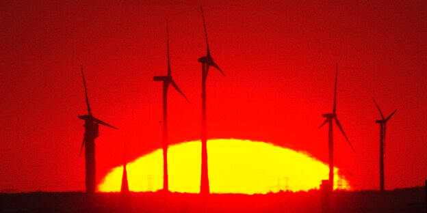 Vor dem rotgefärbten Himmel und der untergehenden Sonne sind Windräder zu erkennen Vor dem rotgefärbten Himmel und der untergehenden Sonne sind Windräder zu erkennen