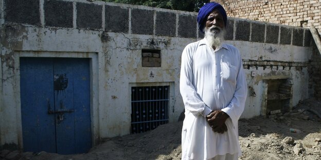 Ein Mann in weißer Kleidung und einem blauen Turban steht vor einem weißen Gebäude