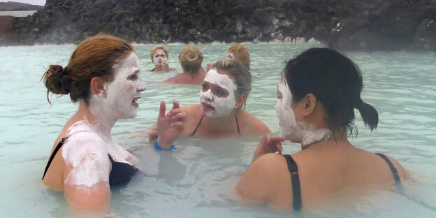 Frauen baden in einer blauen Lagune und tragen weiße Gesichtsmasken Frauen baden in einer blauen Lagune und tragen weiße Gesichtsmasken