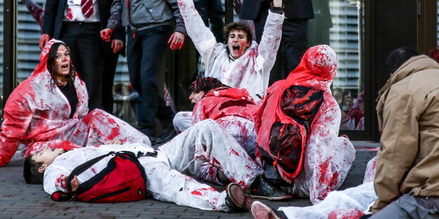 Menschen in rotverschmierten weißen Anzügen vor einem Gebäude Menschen in rotverschmierten weißen Anzügen vor einem Gebäude