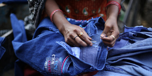 Eine Frau näht eine Jeans mit Stickerei Eine Frau näht eine Jeans mit Stickerei