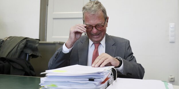 Ein Mann hält seine Brille und guckt auf einen geöffneten Aktenordner Ein Mann hält seine Brille und guckt auf einen geöffneten Aktenordner