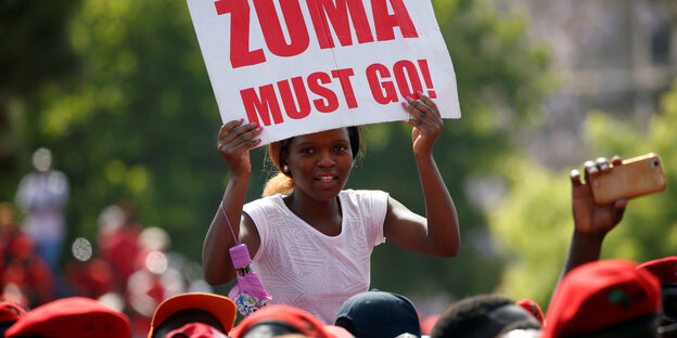 Auf einer Demo hält eine Frau ein Plakat hoch. Auf diesem steht „Zuma must go“ Auf einer Demo hält eine Frau ein Plakat hoch. Auf diesem steht „Zuma must go“