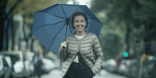 Eva Umlauf steht mit einem Regenschirm inmitten einer Allee Eva Umlauf steht mit einem Regenschirm inmitten einer Allee