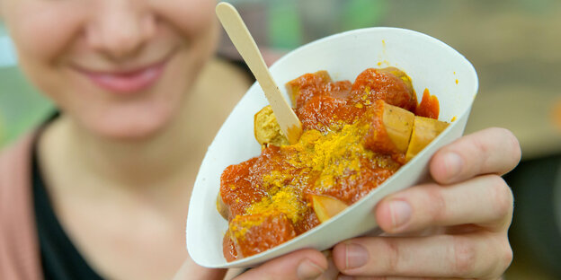 Eine junge Frau hält eine Pappschale mit Currywurst Eine junge Frau hält eine Pappschale mit Currywurst