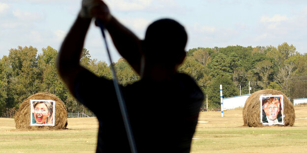 Ein Golfspieler zielt auf zwei Strohballen mit dem Konterfei von Clinton und Trump Ein Golfspieler zielt auf zwei Strohballen mit dem Konterfei von Clinton und Trump