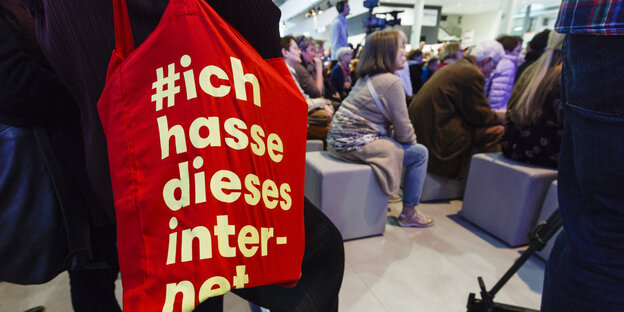 Tasche mit Aufschrift: „Ich hasse dieses Internet“ - auf der Buchmesse, im Hintergrund sitzende Personen bei einer Veranstaltung Tasche mit Aufschrift: „Ich hasse dieses Internet“ - auf der Buchmesse, im Hintergrund sitzende Personen bei einer Veranstaltung