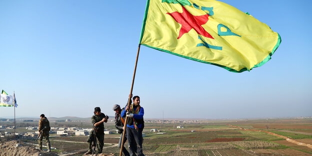 Kurdische Kämpfer halten eine YPG-Fahne hoch Kurdische Kämpfer halten eine YPG-Fahne hoch