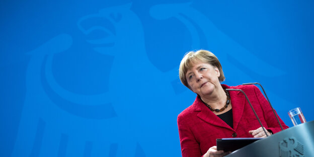 Angela Merkel hinter einem Pult, hinter ihr das Symbol des Bundesadlers Angela Merkel hinter einem Pult, hinter ihr das Symbol des Bundesadlers
