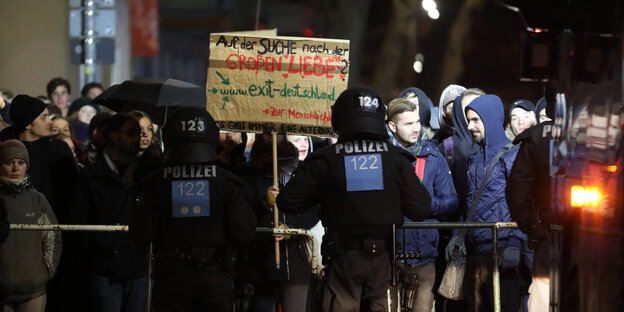 Menschen mit Plakaten stehen vor einer Polizeiabsperrung Menschen mit Plakaten stehen vor einer Polizeiabsperrung
