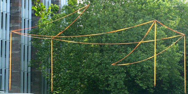 Die Umrisse eines Gebäudes, gezeichnet mit roten Bändern sind vor dem Hintergrund eines grünen Baumes zu sehen Die Umrisse eines Gebäudes, gezeichnet mit roten Bändern sind vor dem Hintergrund eines grünen Baumes zu sehen