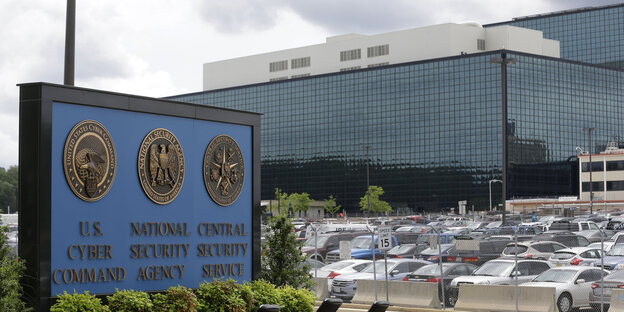 Blick auf die Zentrale der NSA in Fort Meade mit vollem Parkplatz und einer Tafel mit dem Wappen der NSA Blick auf die Zentrale der NSA in Fort Meade mit vollem Parkplatz und einer Tafel mit dem Wappen der NSA