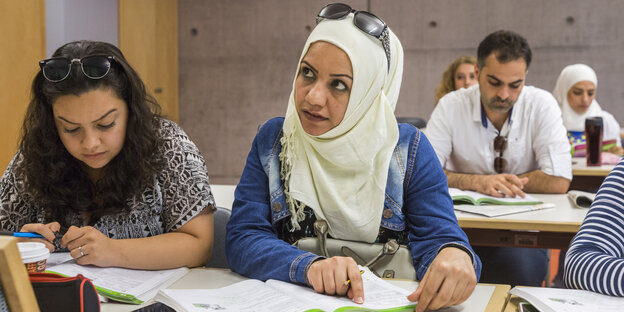 Zahra Alzaher sitzt in einem Klassenraum und legt, während sie hochschaut und nach links blickt, einen Finger auf eine Buchseite Zahra Alzaher sitzt in einem Klassenraum und legt, während sie hochschaut und nach links blickt, einen Finger auf eine Buchseite