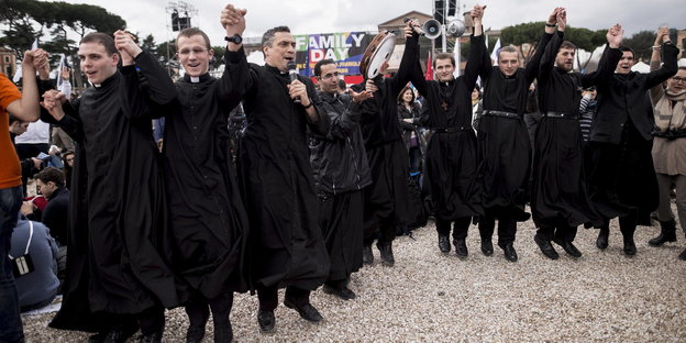 Männer im Priestergewand halten sich an den Händen und hüpfen