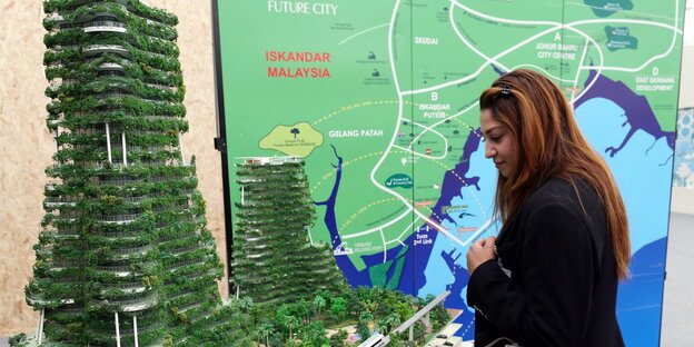 Frau steht vor Modell eines Öko-Hochhauses in Malaysia Frau steht vor Modell eines Öko-Hochhauses in Malaysia