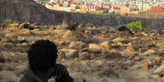 Ein Mann blickt über eine trockene Landschaft und einen Zaun hinweg auf eine Stadt