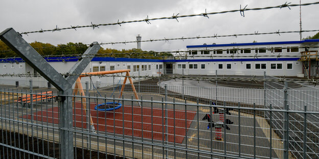 Ein Spielplatz und ein Wohncontainer hinter Stacheldraht Ein Spielplatz und ein Wohncontainer hinter Stacheldraht