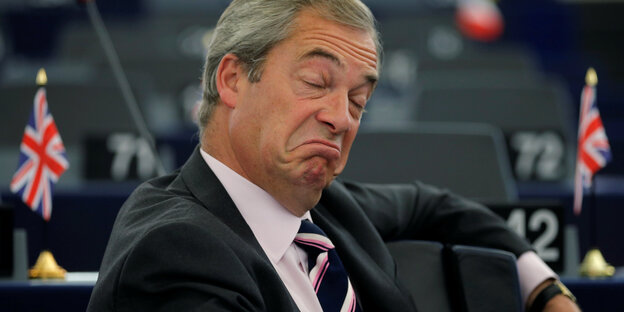 Nigel Farage zieht Mundwinkel mit heruntergezogenen Mundwinkeln und geschlossenen Augen Nigel Farage zieht Mundwinkel mit heruntergezogenen Mundwinkeln und geschlossenen Augen