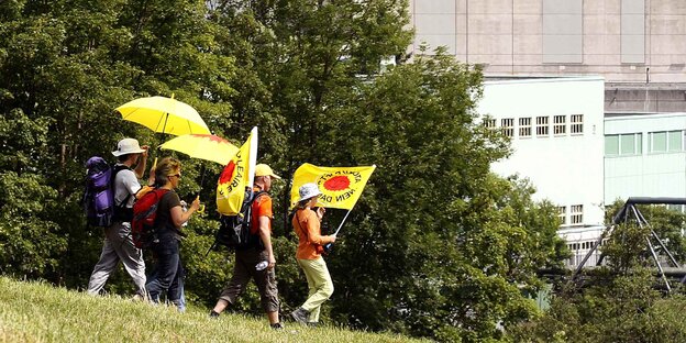 Vier Demonstranten laufen mit Flaggen vor einem Atommeiler Vier Demonstranten laufen mit Flaggen vor einem Atommeiler