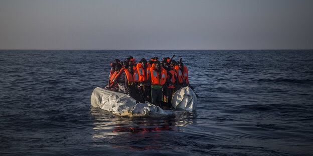Menschen mit Rettungswesten auf einem Schlauchboot im Meer Menschen mit Rettungswesten auf einem Schlauchboot im Meer