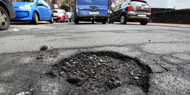 Eine Straße mit einem Loch im Asphalt, dahinter Autos