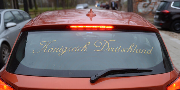 ein rotes Auto auf dessen Heckscheibe „Königreich Deutschland“ steht ein rotes Auto auf dessen Heckscheibe „Königreich Deutschland“ steht