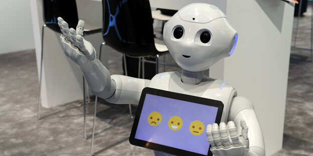 Ein Roboter hält ein Tablet, auf dem drei Smileys zu sehen sind Ein Roboter hält ein Tablet, auf dem drei Smileys zu sehen sind