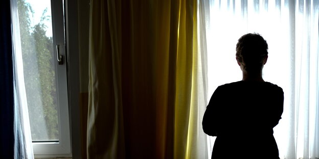 eine junge Frau steht am Fenster mit dem Rücken zum Fotografen eine junge Frau steht am Fenster mit dem Rücken zum Fotografen