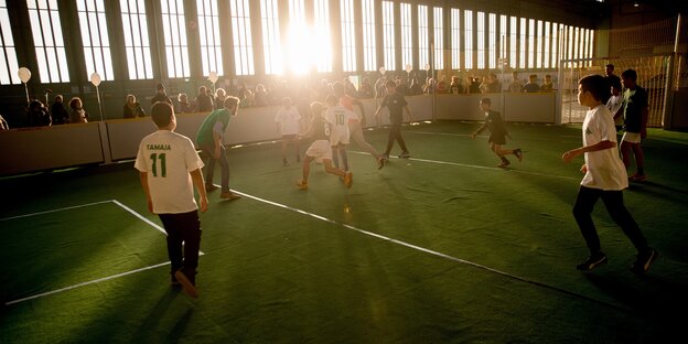 Ein Fußballfeld im Hangar des Tempelhofer Feldes in Berlin. Die Sonne scheint schräg zum Fenster rein. Kinder spielen im Gegenlicht. Ein Fußballfeld im Hangar des Tempelhofer Feldes in Berlin. Die Sonne scheint schräg zum Fenster rein. Kinder spielen im Gegenlicht.