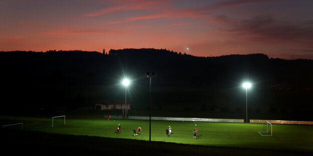 Ein Fußballplatz im Flutlicht, es dämmert, der Himmel ist rosa, die Umgebung schwarz Ein Fußballplatz im Flutlicht, es dämmert, der Himmel ist rosa, die Umgebung schwarz