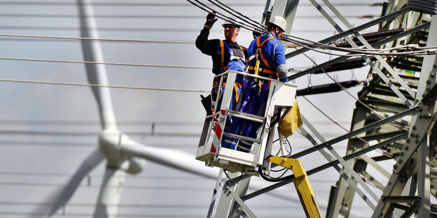 Vor der Kulisse eines Windrades arbeiten zwei Männer an Stromleitungen im Hochspannungsnetz Vor der Kulisse eines Windrades arbeiten zwei Männer an Stromleitungen im Hochspannungsnetz