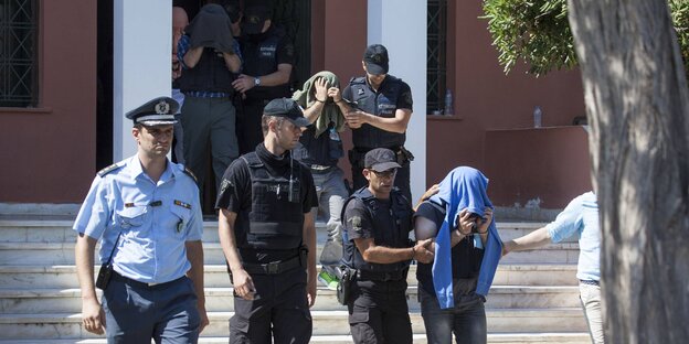 Polizisten führen drei Männer aus einem Gebäude, die mit Pullovern ihre Gesichter verdecken Polizisten führen drei Männer aus einem Gebäude, die mit Pullovern ihre Gesichter verdecken