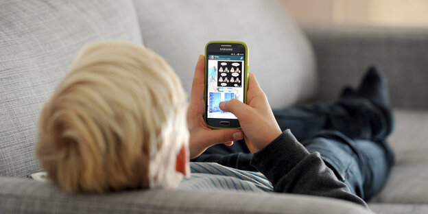 Ein kleiner Junge liegt auf einem Sofa und spielt mit einem Iphone Ein kleiner Junge liegt auf einem Sofa und spielt mit einem Iphone