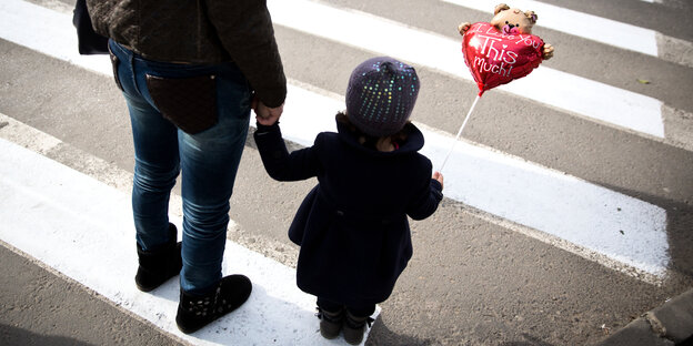 Eine Mutter mit Kind am Zebrastreifen. Das Kind hält einen Luftballon in Herzform Eine Mutter mit Kind am Zebrastreifen. Das Kind hält einen Luftballon in Herzform