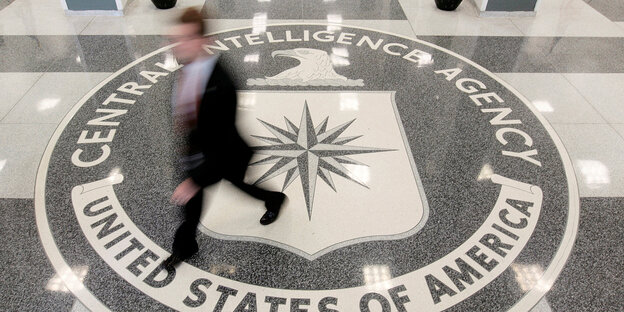 Auf den Boden eingelassenes Wappen der CIA, ein Mann läuft darüber Auf den Boden eingelassenes Wappen der CIA, ein Mann läuft darüber