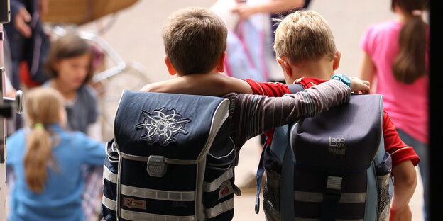 Zwei Kinder umarmen sich mit Schulranzen auf dem Rücken Zwei Kinder umarmen sich mit Schulranzen auf dem Rücken