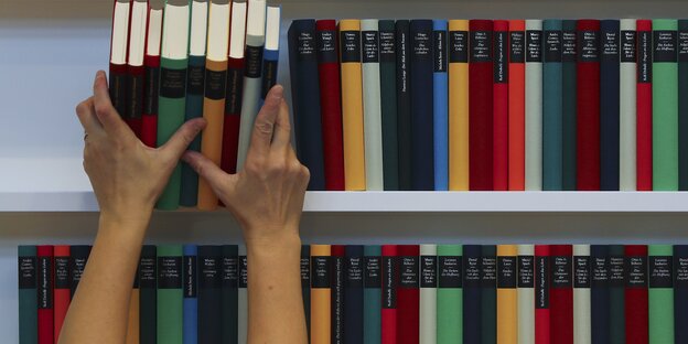 zwei Hände nehmen überkopf einen Stapel Bücher aus einem Bücherregal zwei Hände nehmen überkopf einen Stapel Bücher aus einem Bücherregal