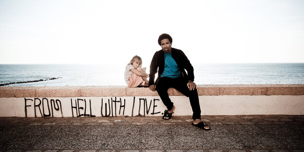 auf einer Mauer steht „FROM HELL WITH LOVE“ daneben sitzen ein kleines Mädchen und ein Mann auf einer Mauer steht „FROM HELL WITH LOVE“ daneben sitzen ein kleines Mädchen und ein Mann