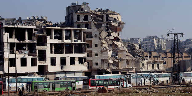 völlig zerstörte Häuser, davor mehrere Busse